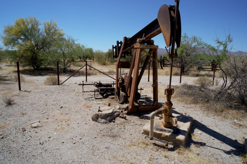 Rusted pumpjack in arid desert setting with sparse vegetation and clear sky.